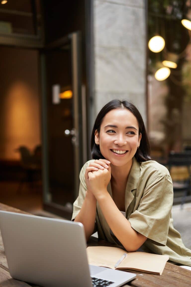 Portrait of asian girl works outdoors in cafe, sits with laptop, studies, smiles happy